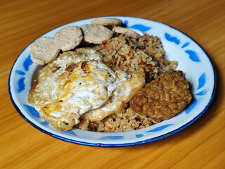 Authentic Indonesian fried rice with sunny side up egg, crackers and fried tempeh on a classic enamel plate.