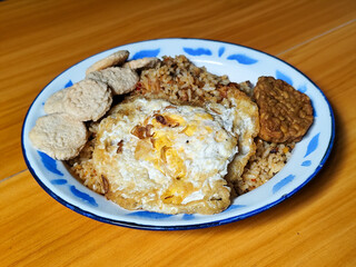 Authentic Indonesian fried rice with sunny side up egg, crackers and fried tempeh on a classic enamel plate.