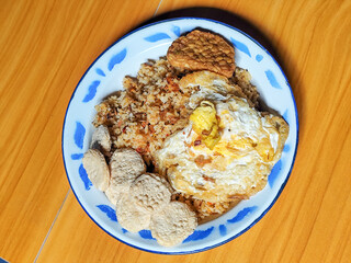 Authentic Indonesian fried rice with sunny side up egg, crackers and fried tempeh on a classic enamel plate.