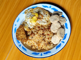 Authentic Indonesian fried rice with sunny side up egg, crackers and fried tempeh on a classic enamel plate.