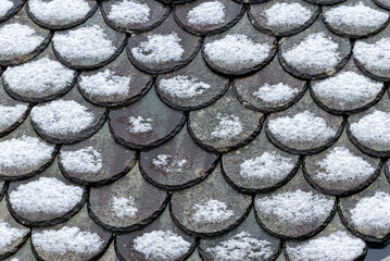 Soft snow covers round slate tiles, transforming the roof into a beautiful winter wonderland during a calm morning.