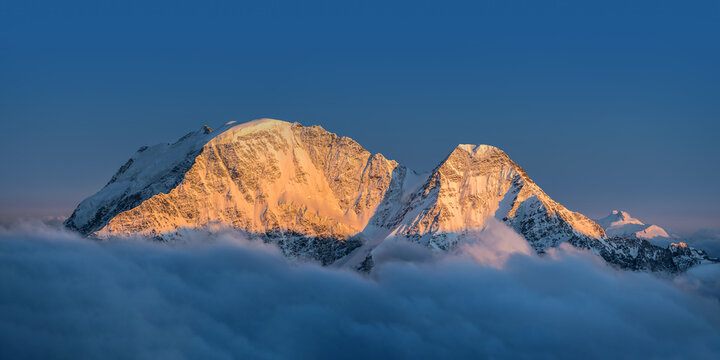 Snowy peaks abobe the cloudes under the clear sky: Donguzorun and Nakra-Tau summits illuminated by the setting sun. View from Elbrus slope, Caucasus mountains, Russia.