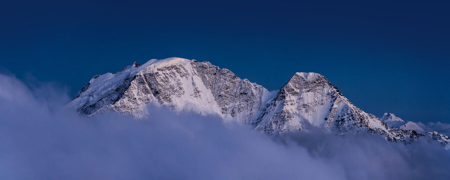 White snowy mountains over the clouds. Caucasian summits Donguz Orun and Nakra after the sunset in twilight.