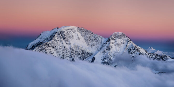 Snowy peaks abobe the cloudes under the clear sky at sunset: Donguzorun and Nakra Tau summits, view from Elbrus slope, Caucasus mountains, Russia.