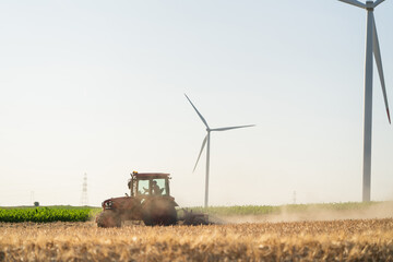 Agricultural tractor on the field with wind turbines