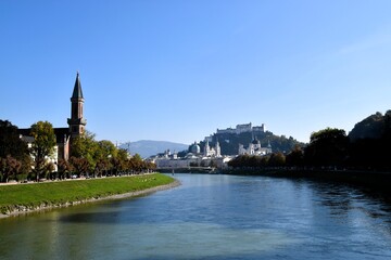 Fototapeta premium Panoramic view of Salzburg's Old Town, Hohensalzburg Fortress, and the Salzach River on a sunny day in Austria.