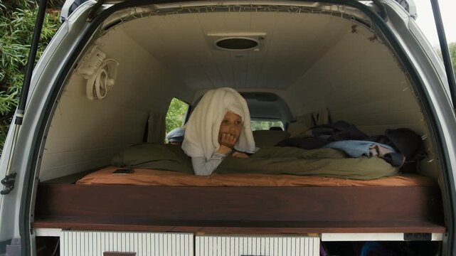 Young child sits comfortably in a camper van, wrapped in a towel, surrounded by bedding