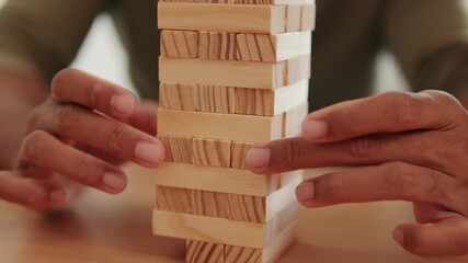 Close up of hands playing Jenga, the classic wooden block tower game. Skill, strategy, and steady hands are required for this game of precision. Perfect for family game night.