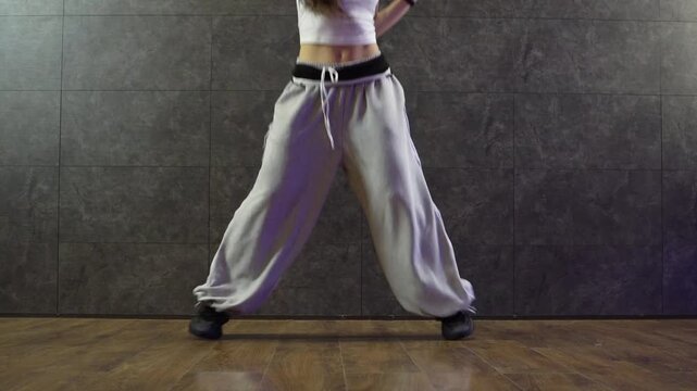young girl in sweatpants dancing hip hop with her feet in a dance hall, close-up of choreographer's feet in motion