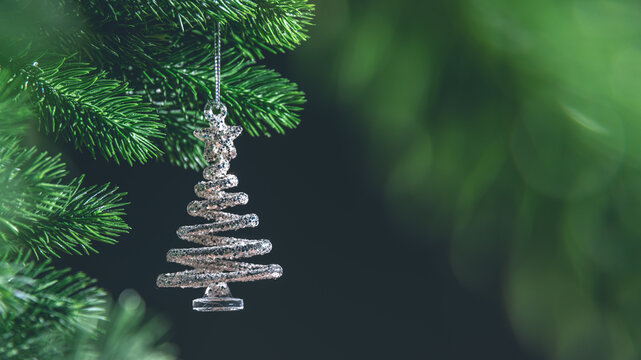 Fototapeta Silver spiral christmas tree ornament hanging from a green branch on dark background, creating a festive and magical atmosphere with copy space