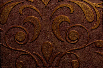 Dark brown paper/fabric with a decorative plaster texture on the surface, featuring a pattern of curling leaves and flowers, for interior design with an aged effect