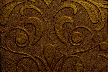 Golden bronze wallpaper with decorative plaster texture featuring a pattern of curling leaves and flowers for interior design