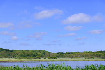 A brackish lagoon called Poroto-numa located within the Poroto Marsh in Hamanaka, Hokkaido, Japan. The lagoon is surrounded by wetlands and aquatic plants, creating a serene natural landscape under a 