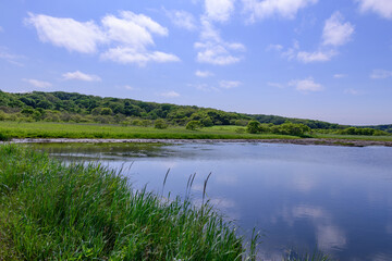 A brackish lagoon called Poroto-numa located within the Poroto Marsh in Hamanaka, Hokkaido, Japan. The lagoon is surrounded by wetlands and aquatic plants, creating a serene natural landscape under a 