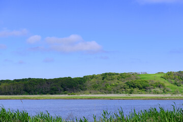 A brackish lagoon called Poroto-numa located within the Poroto Marsh in Hamanaka, Hokkaido, Japan. The lagoon is surrounded by wetlands and aquatic plants, creating a serene natural landscape under a 