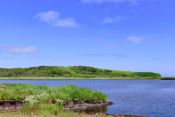 A brackish lagoon called Poroto-numa located within the Poroto Marsh in Hamanaka, Hokkaido, Japan. The lagoon is surrounded by wetlands and aquatic plants, creating a serene natural landscape under a 