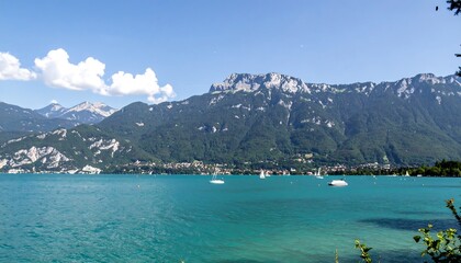 Obraz premium Picturesque alpine lake with mountains in the background, featuring a serene turquoise water and sailboats dotting the calm surface.
