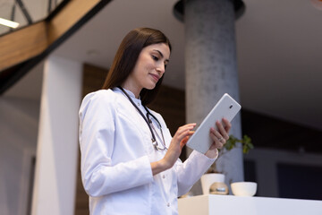 Female physician reviewing digital tablet, walking hospital corridor, managing medical records with professional expertise, embracing healthcare technology