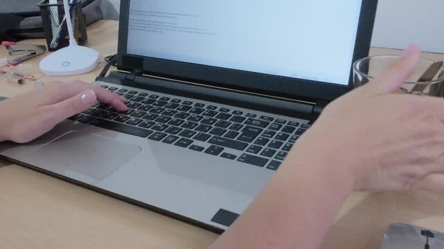 Modern technology in use: hands typing on a laptop displaying Hebrew script.