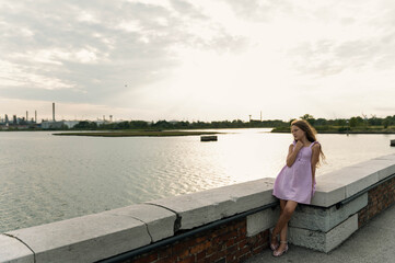 Full body of a young girl in a purple dress resting on the side of Ponte della Libertà in Venice, Italy, looking toward the lagoon.
