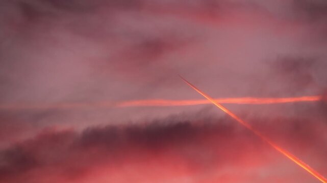 A vibrant sunset sky with shades of orange, pink, and purple clouds. A jet contrail cuts through the scene, adding a dynamic element to the tranquil atmosphere.