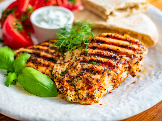 Grilled chicken breast, tomatoes, pita bread and tzatziki sauce on wooden table