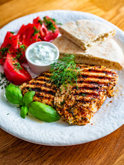 Grilled chicken breast, tomatoes, pita bread and tzatziki sauce on wooden table