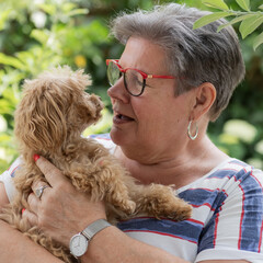 Porträt einer Seniorin mit einem Maltipoo auf dem Arm