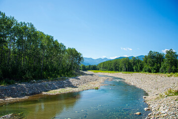 Scenic Mountain  River Flowing Through Lush Green Forest Under Blue Sky