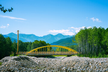 Yellow Bridge over a Rocky River with Mountains in the Background