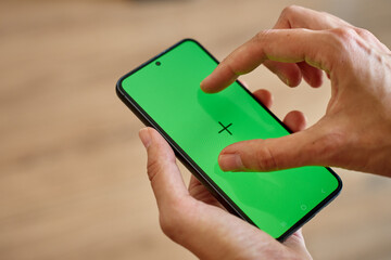 Hands holding smartphone and touching display with green screen and tracking markers. Person using mobile phone, close up