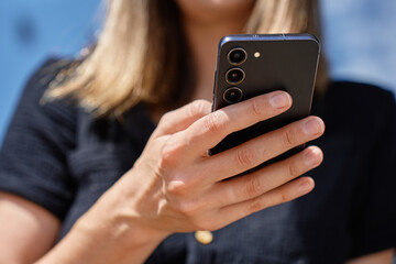 Woman using smartphone. Close-up of female hand holding modern mobile phone outdoors in daylight. Using technology in daily life and communication concept