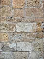 Closeup of weathered stone wall surface made of rectangular blocks showing cracks, natural textures and rustic details
