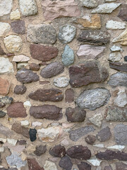 Closeup of an old stone wall with aged surface and mortar, featuring irregular blocks in brown, grey and beige tones typical of historic architecture