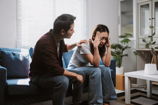 Young man comforting his sad girlfriend while sitting together on the sofa, offering support and compassion during a difficult moment at home