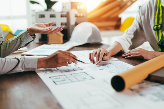 Two engineers analyzing blueprints and engaging in discussion about a new building project within the office environment