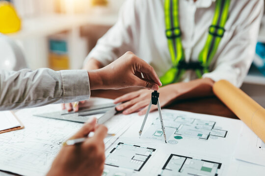 Team of architects using compass and set square working together on construction blueprint at office desk