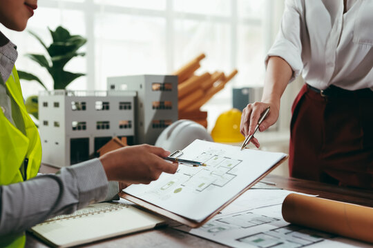 Two architects analyzing blueprints and engaging in a detailed discussion about a building project within the office environment