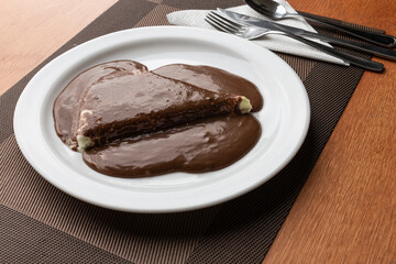 Pizza doce de sorvete de baunilha com calda de chocolate, servido em um prato branco em uma mesa de madeira.