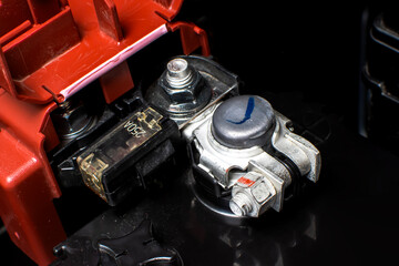 Close-up of a car battery positive terminal in red with fuse and connector, showing electrical connections and power distribution components in an automotive system