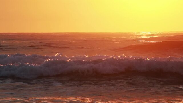 Ocean surf at dawn, waves close-up. Background, man surfing. Sky is golden, yellow-orange and beautifully reflected in water