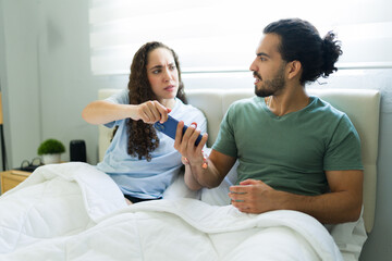 Woman grabbing her boyfriend’s phone while he resists during a dispute in bed