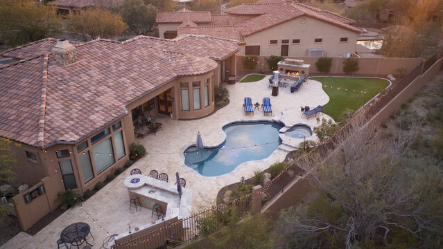 A desert landscaped backyard featuring a travertine tile pool deck, fireplace and outdoor kitchen.