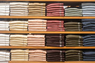Cloths in various base color tone are folded on the shelf in clothing store. Fashion cloth object photo, close-up and selective focus.	
