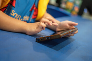 Close-up at a kid hand is holding smartphone during watching the screen and placed hand on table.