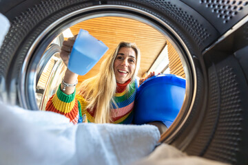 Blonde European woman leaning to look inside laundromat washing machine while doing her laundry