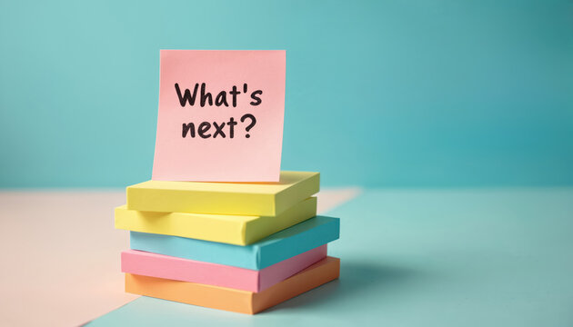 Stack of colorful sticky notes with phrase What next in pyramid formation. Light blue background contrasts with vibrant colors of notes. Business planning and strategy concept.