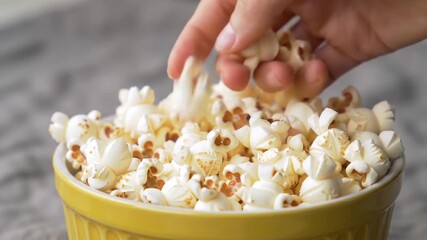Yellow bowl of popcorn with hand reaching in, perfect for movie nights, snack advertising, cinema themes, and social media content.