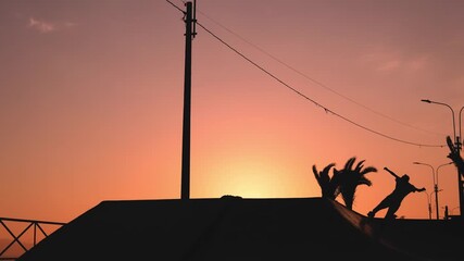 Skater showing his skills on a rooftop ramp at sunset, not recognizable.