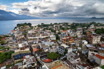 Fototapeta premium Aerial panoramic view of Lake Atitlán and San Pedro in Guatemala with volcanic mountains, lush green landscape, and dramatic sky over Central America